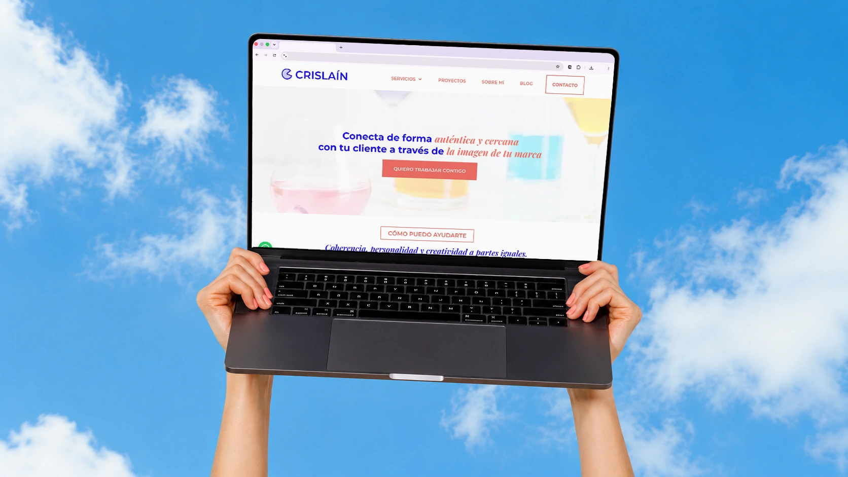 Dos manos sostienen un ordenador portátil frente a un cielo azul con nubes. En la pantalla del ordenador portátil se ve la página de inicio de la web de CRISLAIN en español.